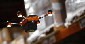 Autonomous Corvus drone flying through warehouse aisles while scanning inventory on high storage shelves